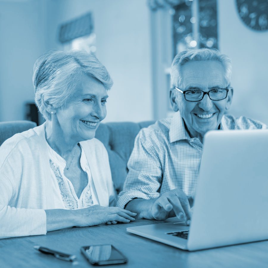 An older couple at the kitchen table, answering questions together on a laptop